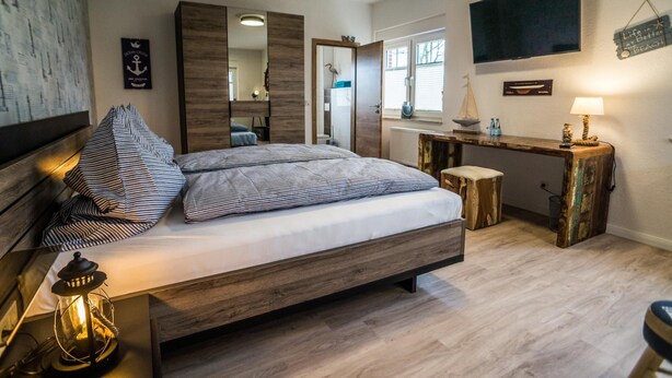 Un dormitorio con cama, mesita de noche, lámpara y espejo.