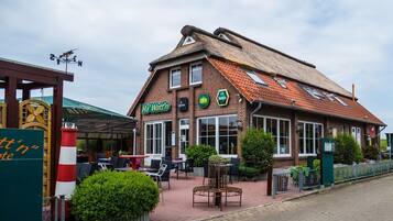 A brick building with a thatched roof, a sign reading "Ha' Watt'n", and outdoor seating.