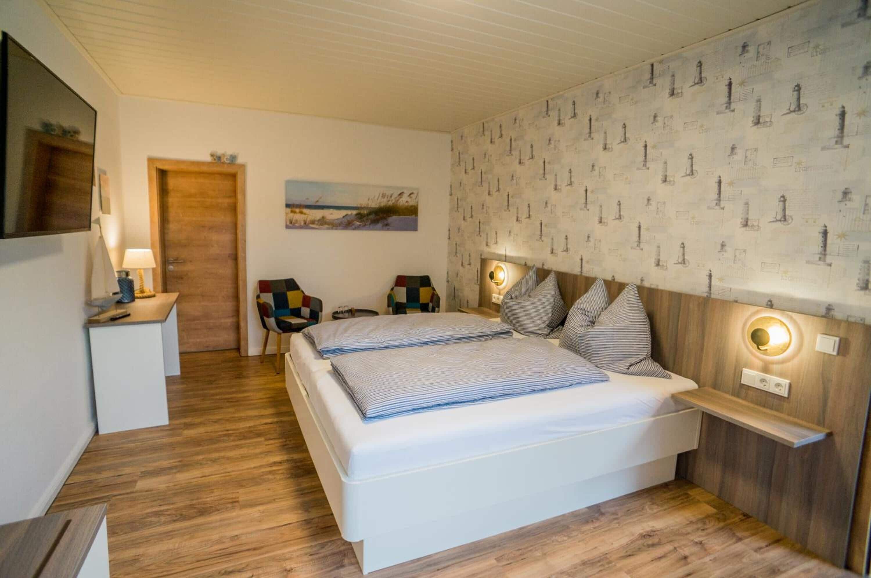 A bedroom with a bed, bedside tables, a nightstand, a chair, a lamp, and a wall with a nautical pattern.