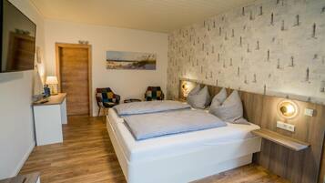 A bedroom with a bed, bedside tables, a nightstand, a chair, a lamp, and a wall with a nautical pattern.