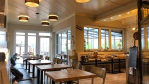 Un restaurante con varias mesas y bancos, ventanas amplias e iluminación colgante.