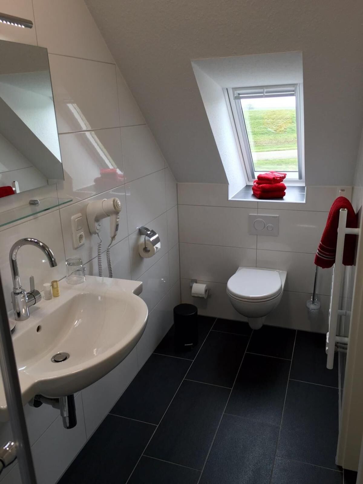 A modern bathroom with a white sink, a toilet, and a small window with a view of the outdoors.