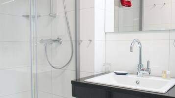 Ein modernes Badezimmer mit einer Duschkabine, einem weißen Waschbecken und einer schwarzen Arbeitsplatte sowie einem Spiegel über dem Waschbecken.