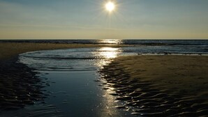Uma praia com o sol refletindo na água, criando um efeito cintilante na areia.