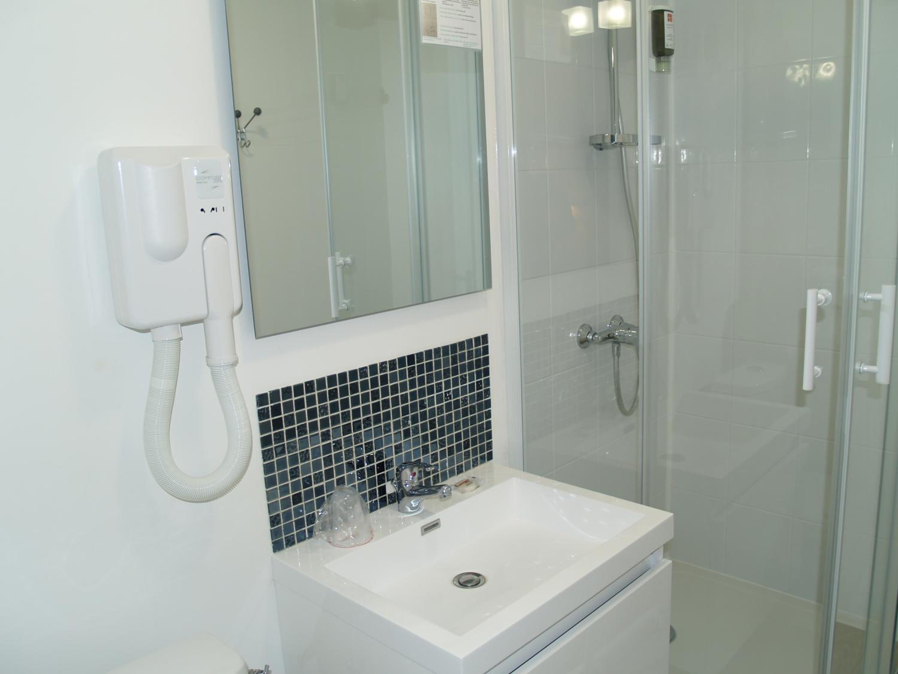 A bathroom with a white sink, a mirror, a glass shower enclosure, and a white telephone.