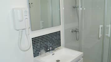 A bathroom with a white sink, a mirror, a glass shower enclosure, and a white telephone.
