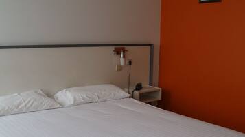A neatly made bed in a hotel room with a plain wall and a single framed picture.