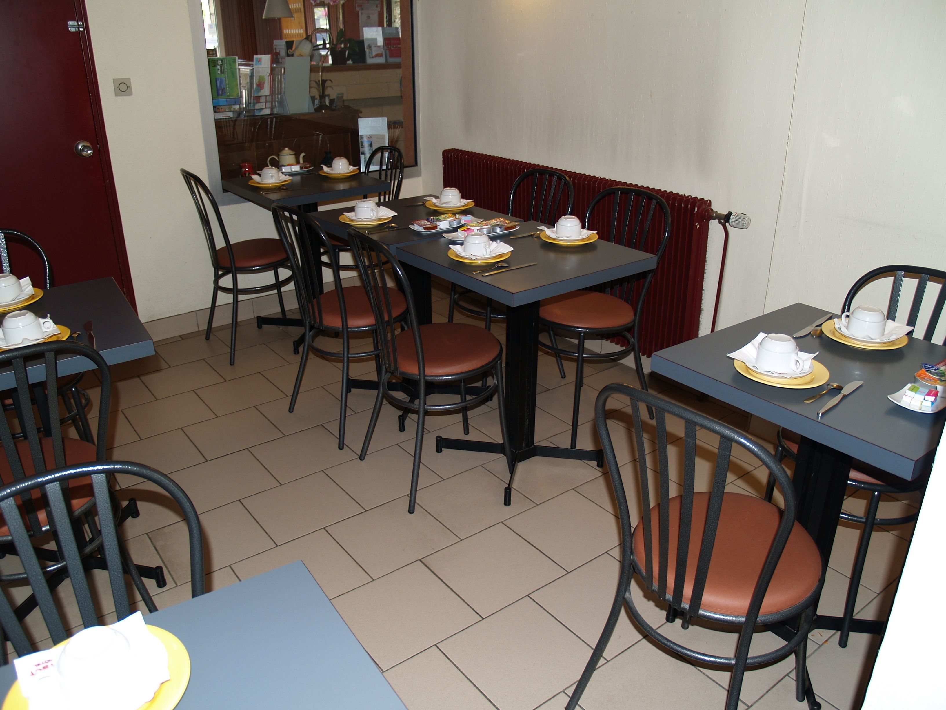 Een eetruimte met meerdere tafels en stoelen, elk voorzien van witte kopjes en schotels.