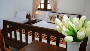 A bedroom with a wooden bed, a bedside table, a nightstand, a lamp, and a vase with white flowers. - Muduna Walawwa Resort (Kandy)
