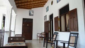 A covered porch with wooden benches and chairs, a wooden door, and a wall with decorative panels and a hanging light fixture. - Muduna Walawwa Resort (Kandy)