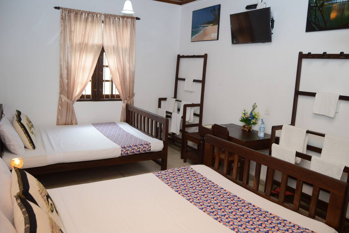 A hotel room with two beds, a wooden chair, a small table, a TV, and a painting on the wall.
