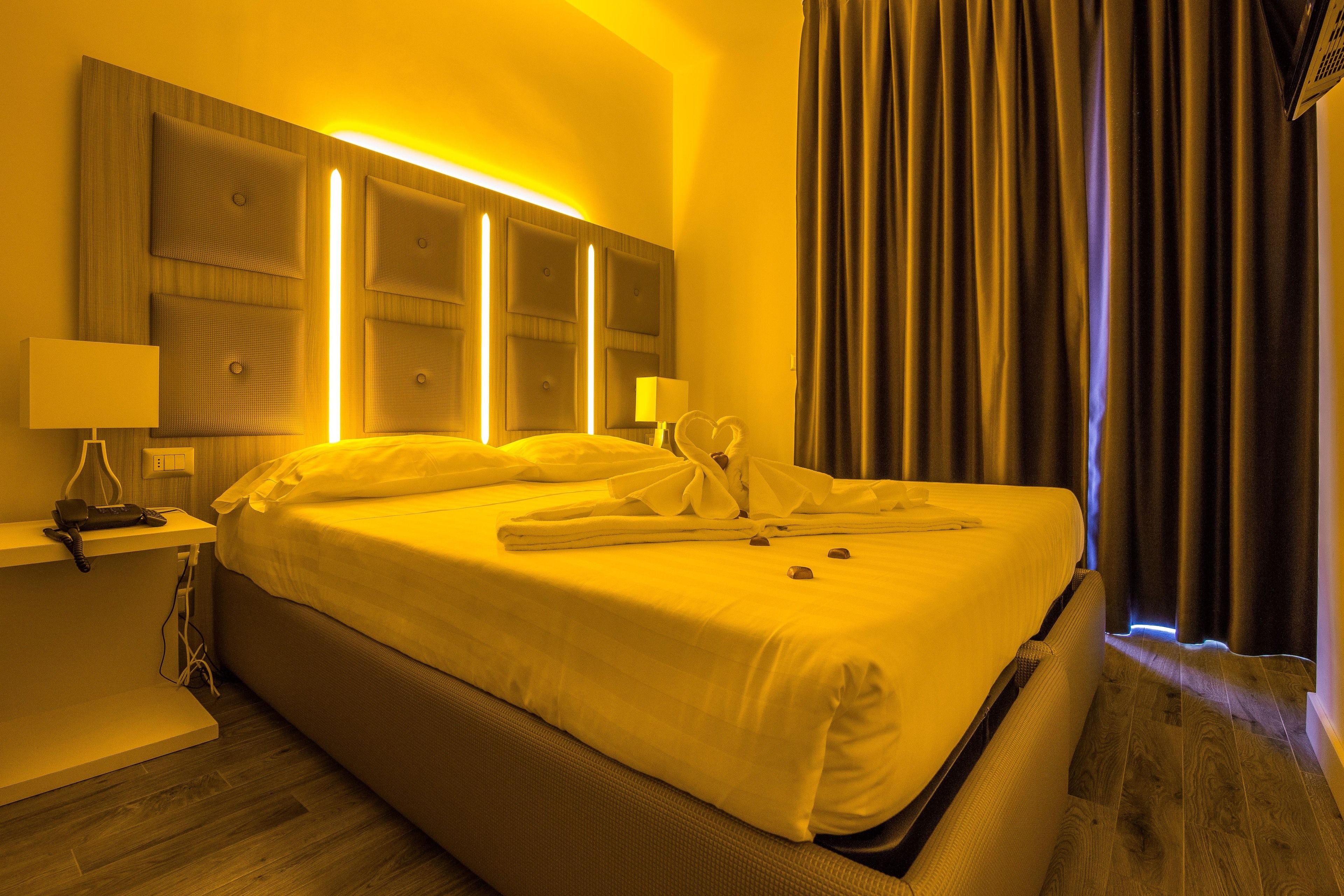 A hotel room with a large bed, bedside lamps, a wooden headboard, and a curtain.