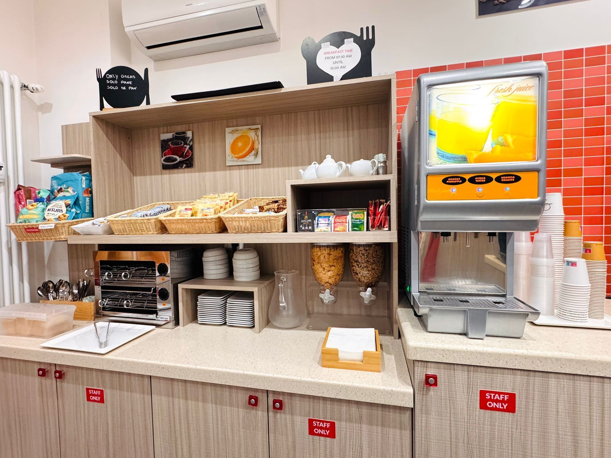 A breakfast counter with a coffee machine, baskets of bread and pastries, and a sign indicating breakfast time.