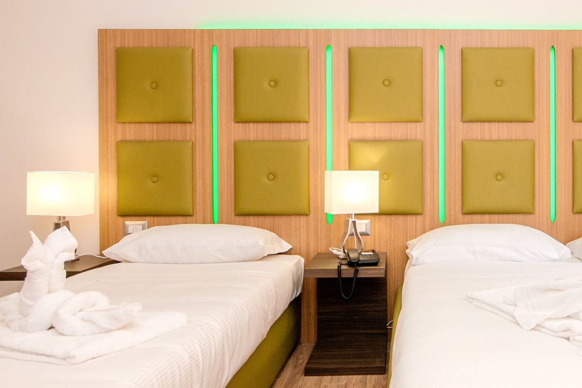 A hotel room with two beds, a wooden headboard with square panels, bedside lamps, and neatly folded towels.