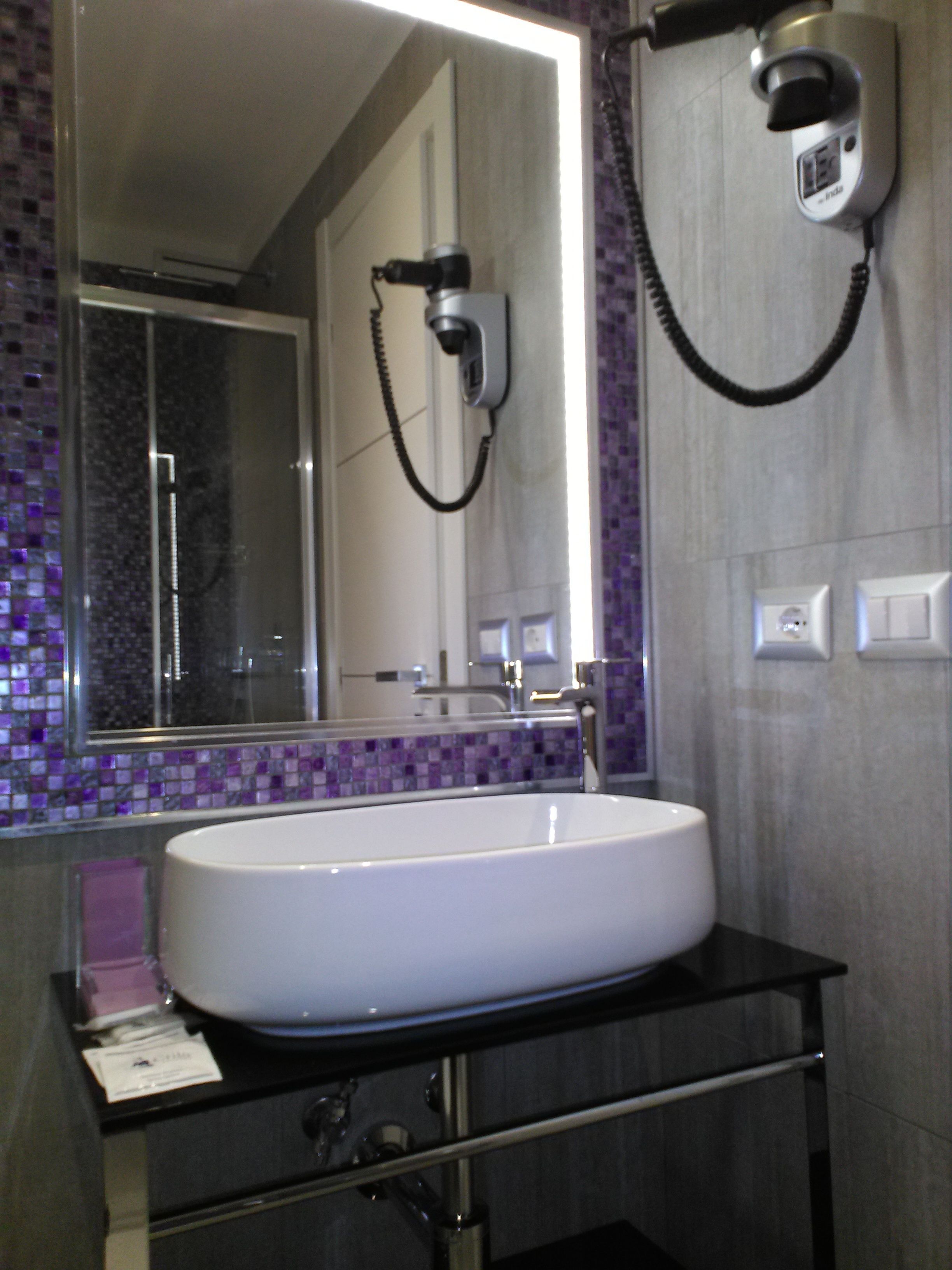 A bathroom with a white sink, a mirror, and a hairdryer mounted on the wall.