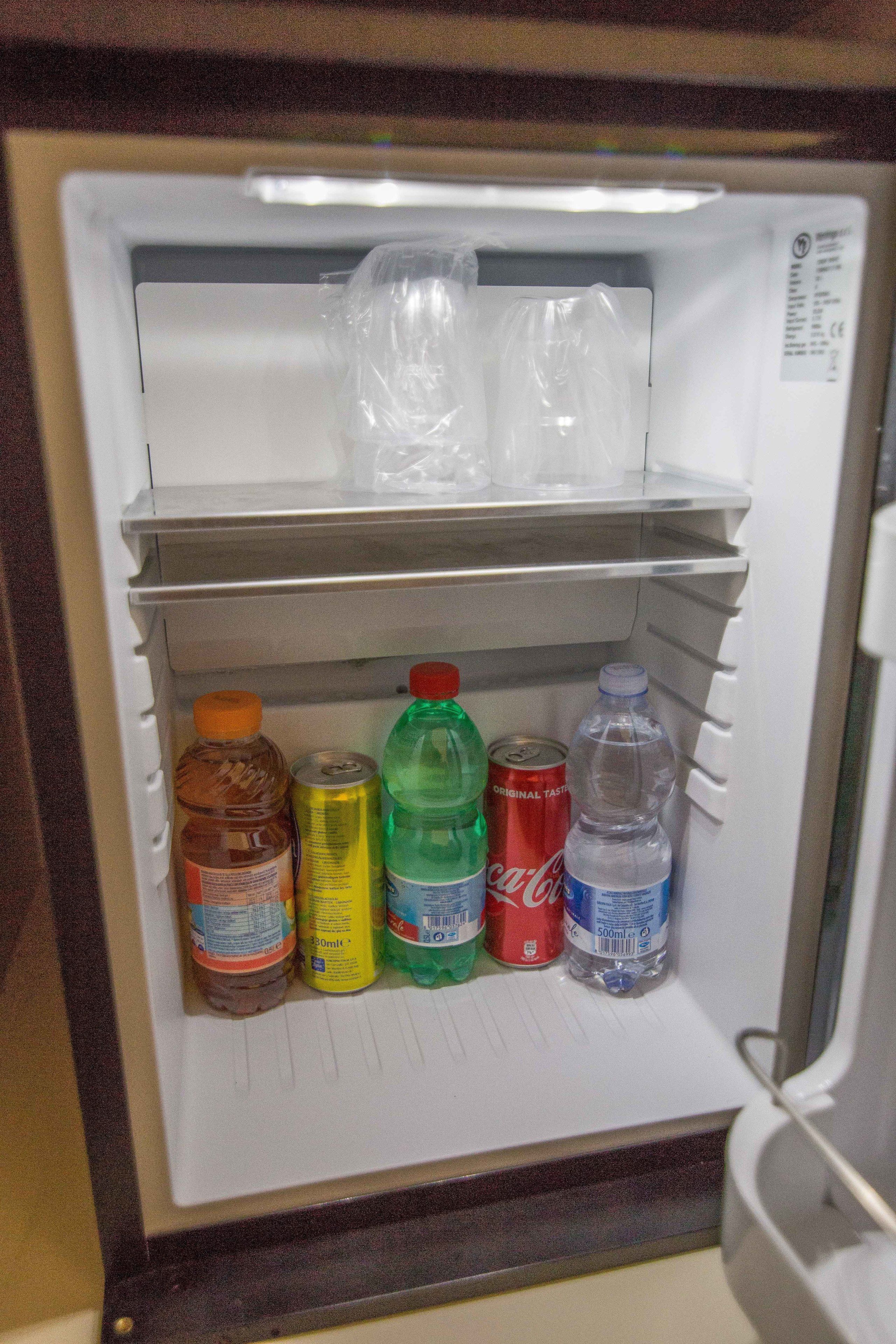 A refrigerator with shelves containing various beverages including a bottle of water, a can of soda, and a bottle of juice.