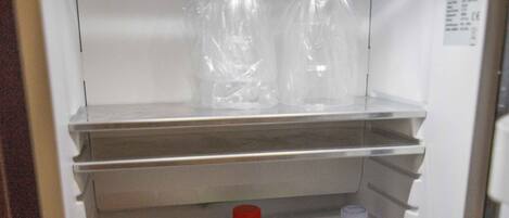 A refrigerator with shelves containing various beverages including a bottle of water, a can of soda, and a bottle of juice.