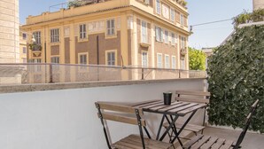 A balcony with a wooden table and chairs, overlooking a building with multiple windows and balconies. - Vatican Relais Rome (Rome)