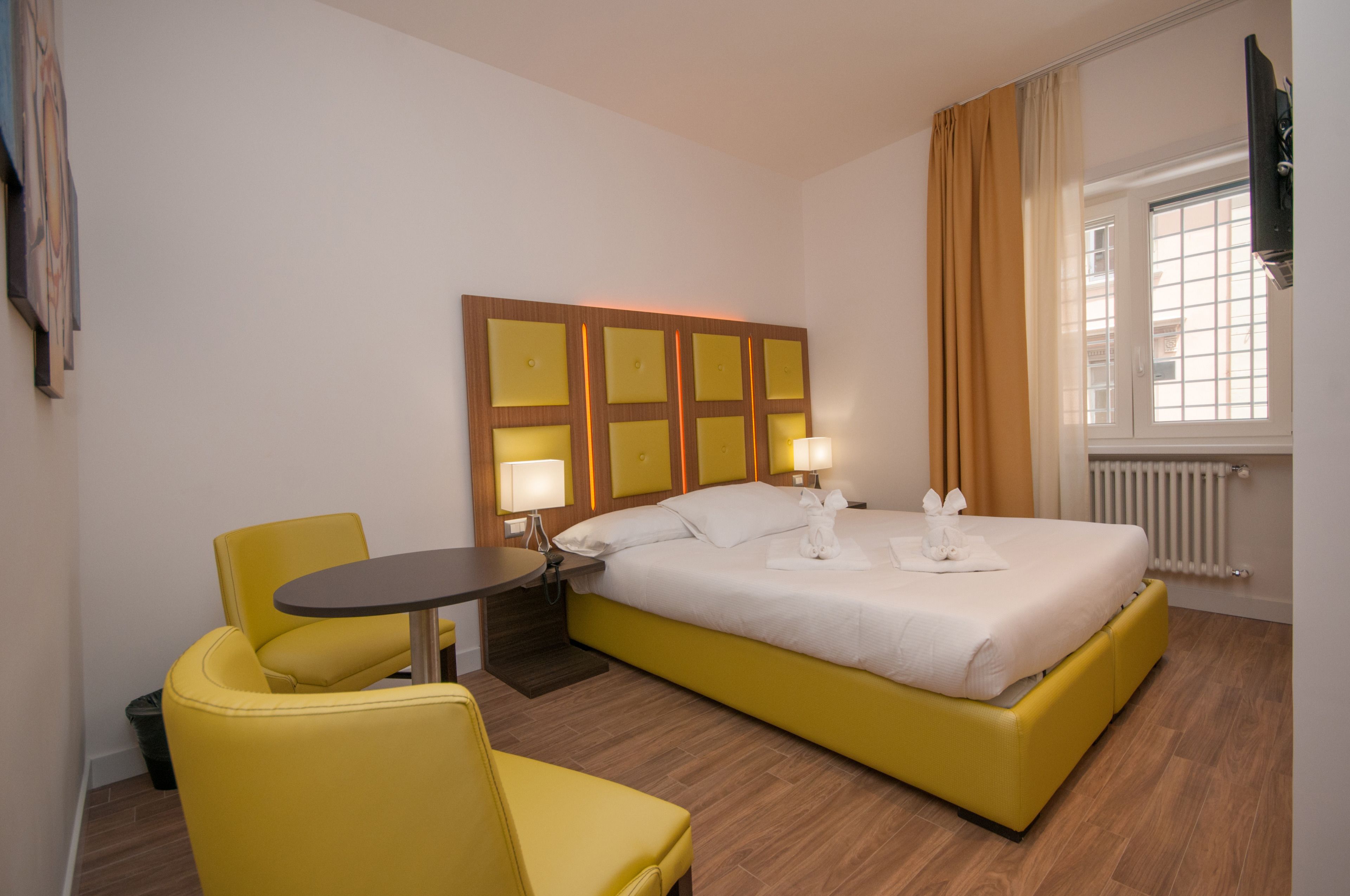 Una habitación de hotel con una cama grande, una mesita pequeña y un sillón amarillo.