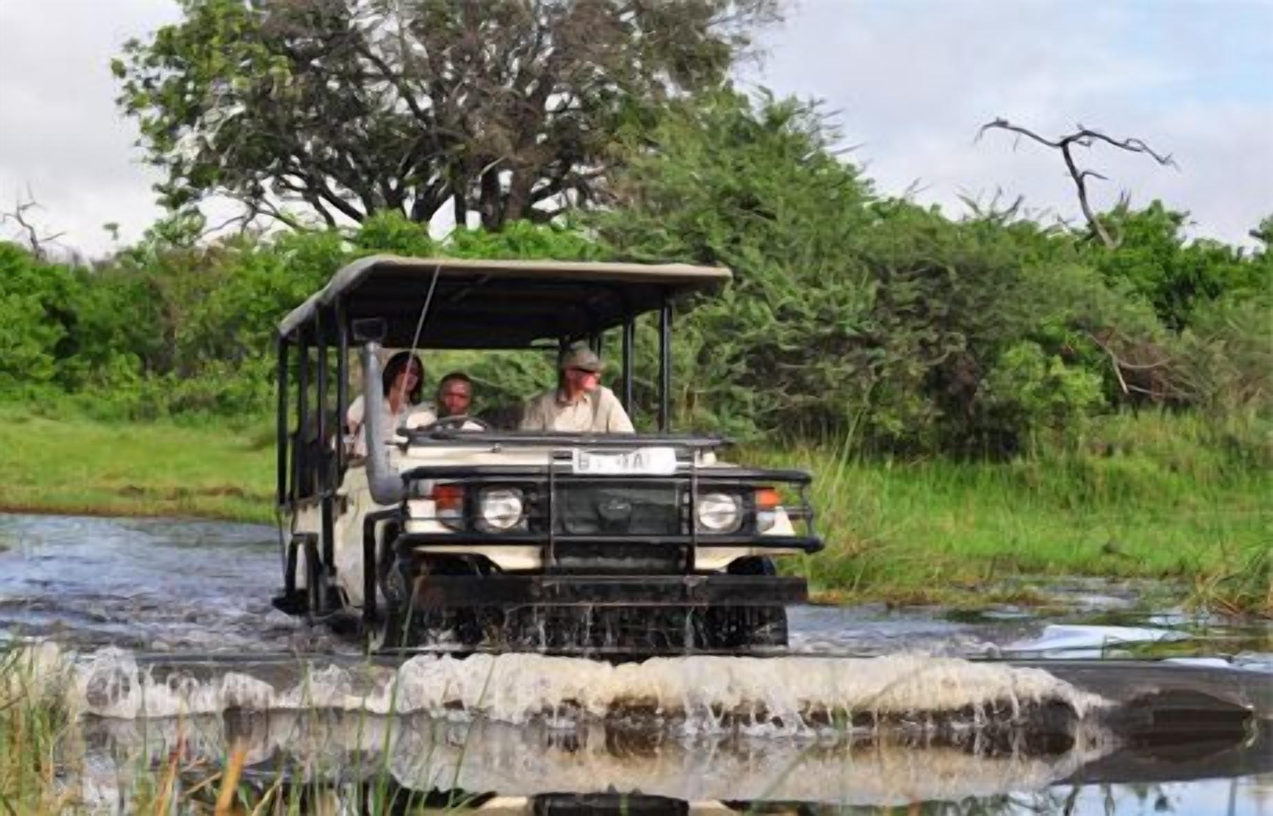 A safari vehicle crossing a shallow water body with passengers.