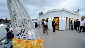 Un espacio en la azotea con un edificio blanco, gente reunida y una silla con cojín floral.