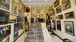 Un amplio pasillo con escaleras de mármol, numerosas obras de arte enmarcadas en las paredes y un espejo central ornamentado.