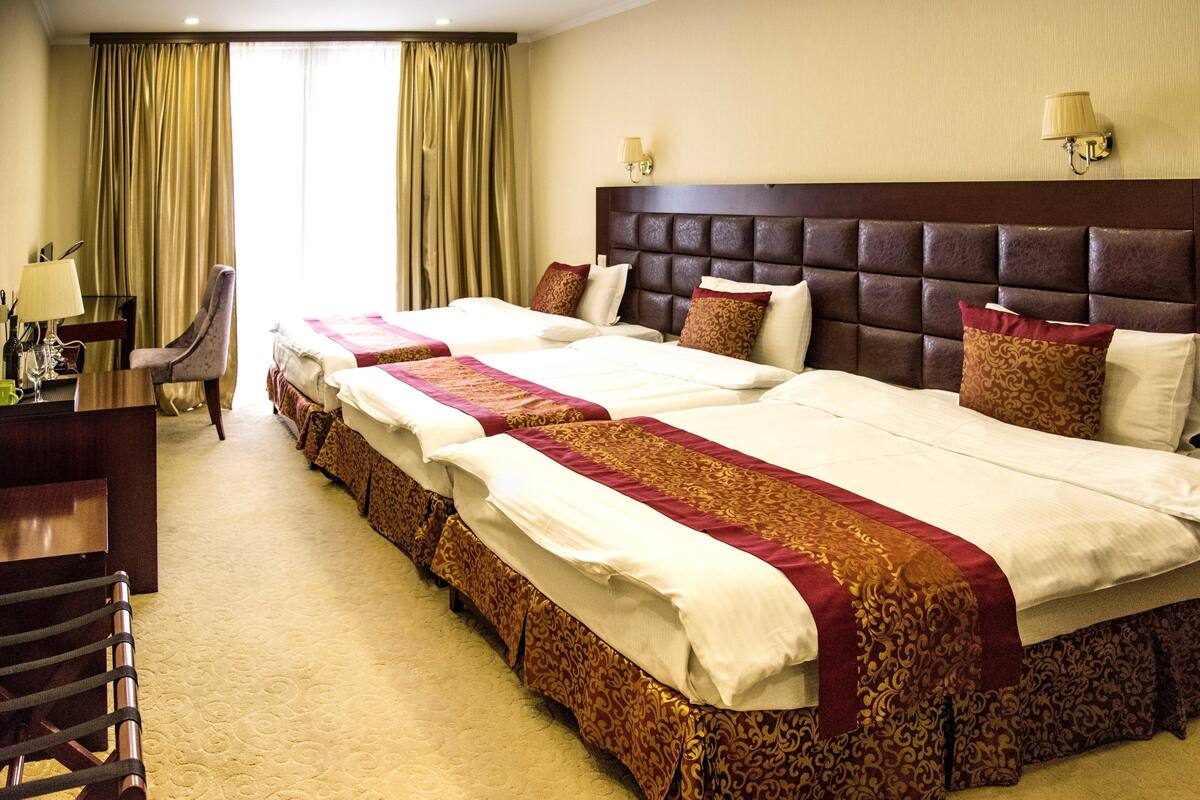 A hotel room with three beds, a desk, and a chair.
