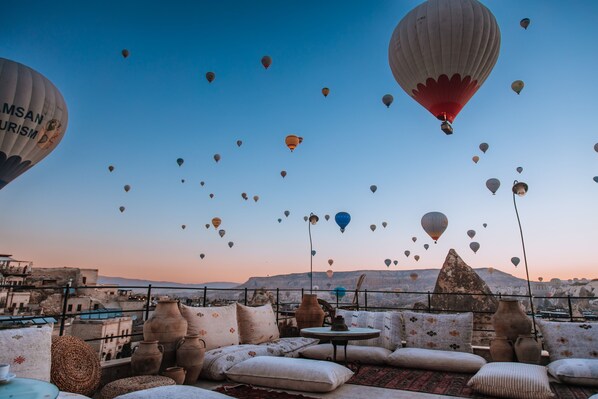 A rooftop terrace with multiple hot air balloons in the sky, a view of the cityscape, and traditional pottery and cushions. - Taskonak Hotel (Nevsehir)
