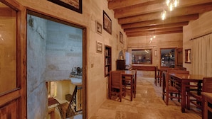 A spacious dining area with wooden tables and chairs, a stone floor, and a view through a large doorway to another room. - Taskonak Hotel (Nevsehir)