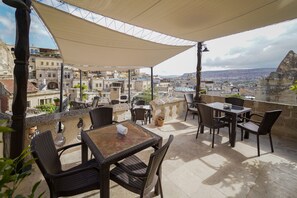 An outdoor patio with wicker furniture, a table with a napkin, and a view of the cityscape. - Taskonak Hotel (Nevsehir)