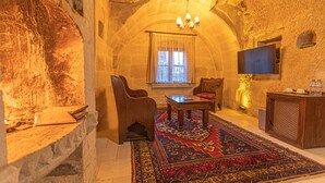 A cozy room with a stone wall, a wooden table, a sofa, a patterned rug, and a television. - Taskonak Hotel (Nevsehir)