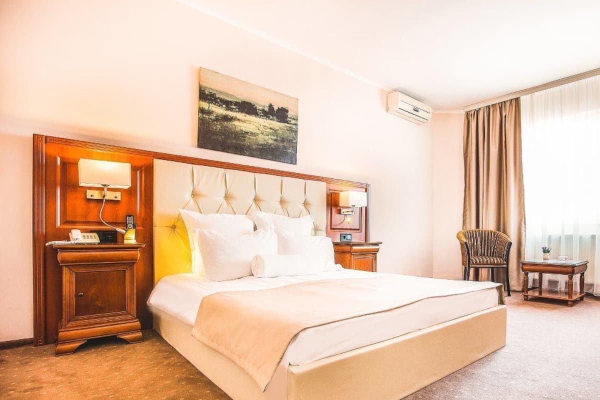 A hotel room with a large bed, bedside tables, a chair, and a window with curtains.