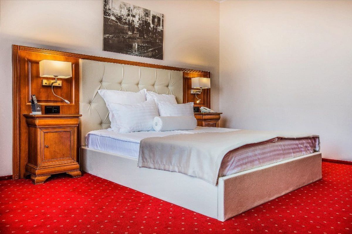 A hotel room with a large bed, two bedside tables, a headboard, and a red carpet.
