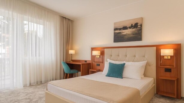 A hotel room with a large bed, a desk, a chair, and a painting on the wall.