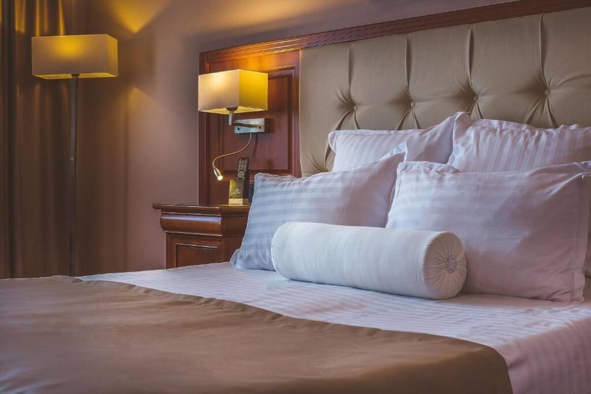 A hotel room with a large bed, a wooden nightstand, a lamp, and a wall-mounted light fixture.