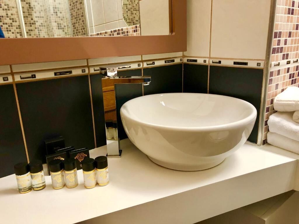 Ein Badezimmer mit einem großen weißen Waschbecken, einem Spiegel und einer gefliesten Rückwand.