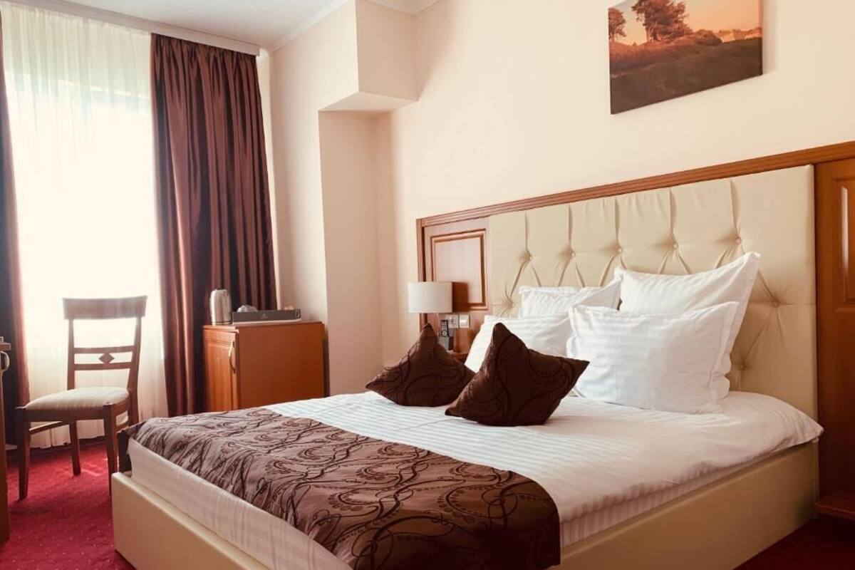 A hotel room with a large bed, a desk, a chair, and a painting on the wall.