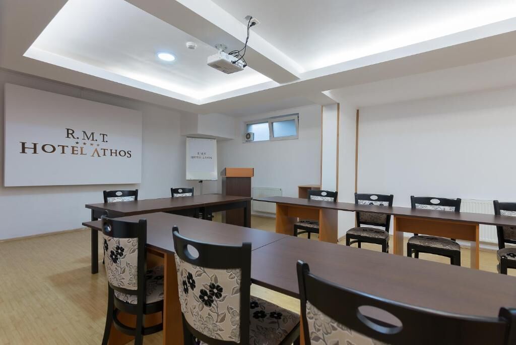 Un salón de conferencias con una larga mesa y sillas, una pantalla de proyector y un cartel que indica HOTEL ATHOS R.M.T.