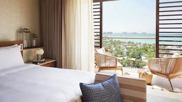 Hotelkamer met een groot bed, nachtkastje met lamp, vaas met bloemen en uitzicht op strand en stadsbeeld.