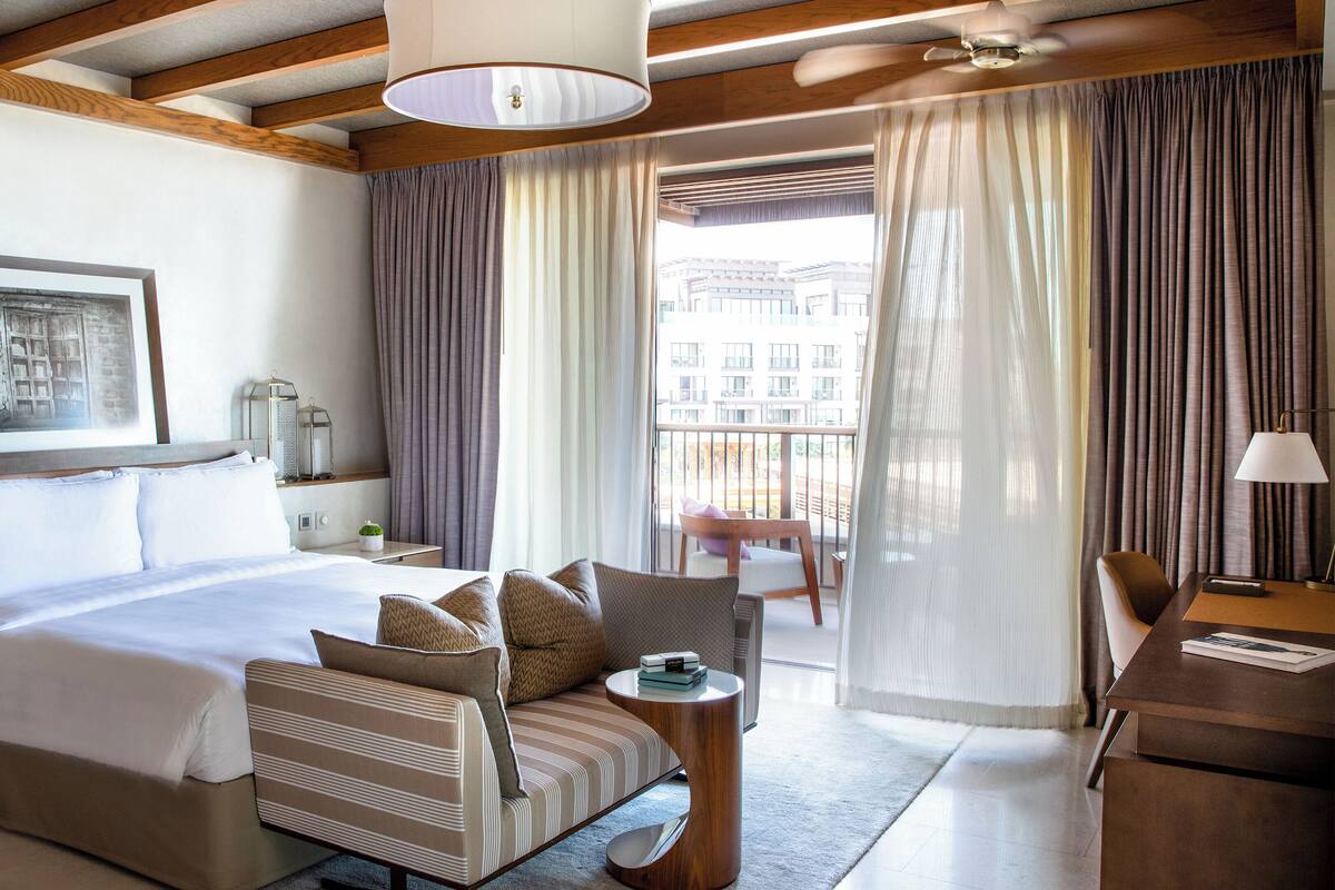 Habitación de hotel con cama, sofá, escritorio, silla y balcón con cortinas.