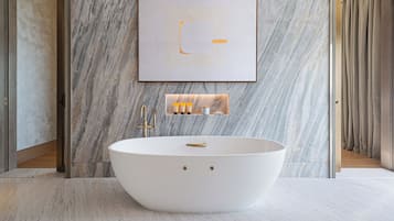 Un baño moderno con una bañera independiente, paredes de mármol y una obra enmarcada sobre el lavabo.