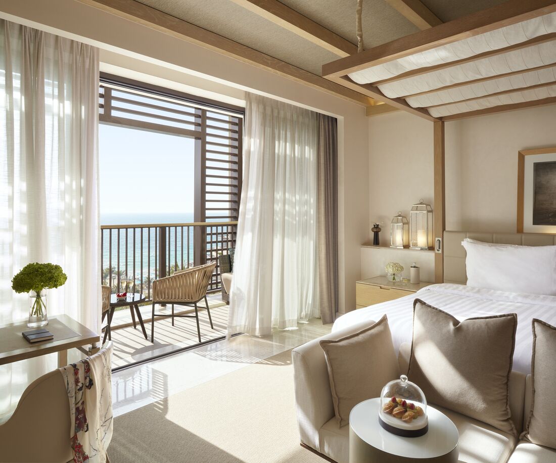 A hotel room with a balcony, a bed, a desk, and a seating area.