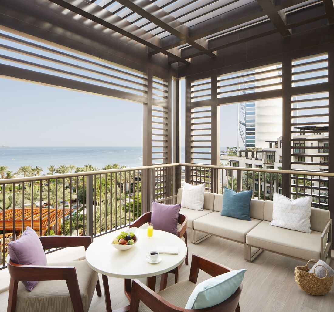 Un balcon avec vue sur l’océan, un ensemble de canapés, une table à manger avec des chaises et un panier.