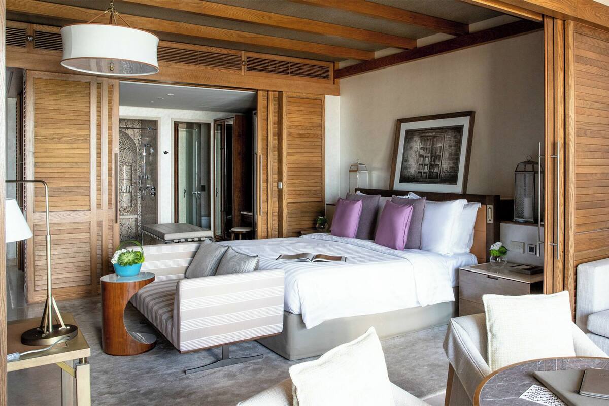 Un dormitorio moderno con una cama grande, una mesita de noche, una silla y una pequeña mesa con una lámpara.