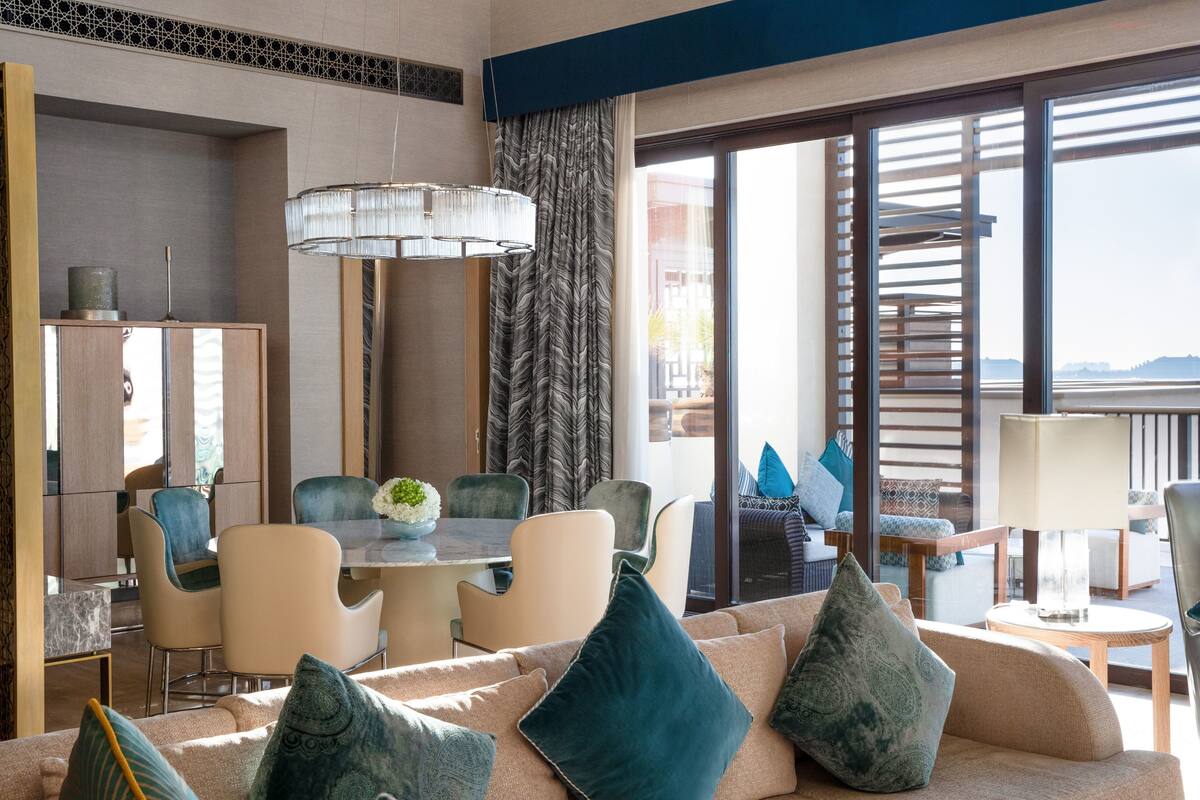 Una habitación de hotel moderna con zona de comedor, un conjunto de sofás y vistas al exterior.