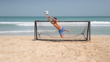 Un joueur de volleyball de plage, vêtu d’un short bleu, saute pour frapper une balle près d’un filet de volleyball.