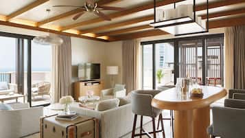 A spacious living room with a large TV, comfortable seating, a bar area, and a view of the ocean.