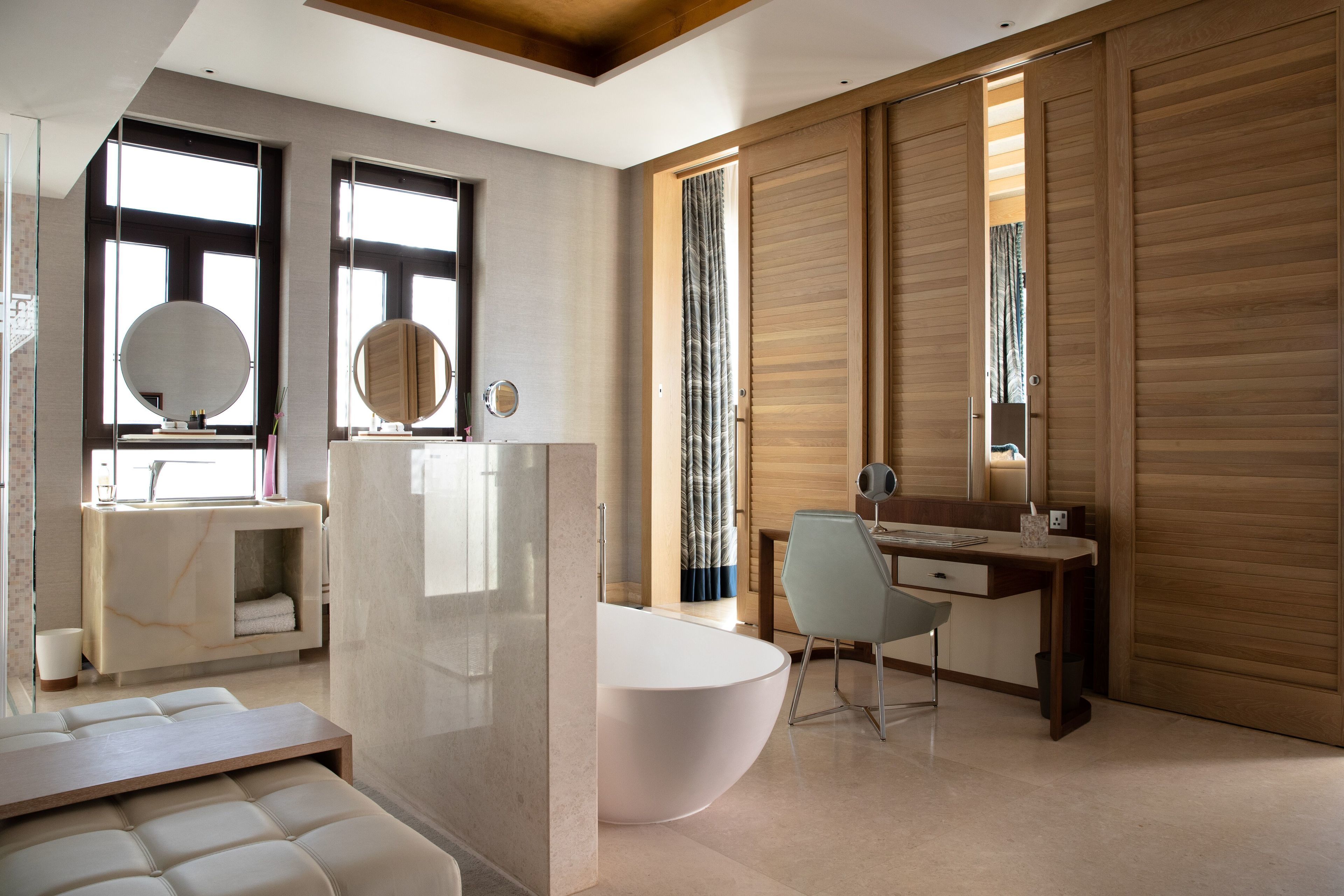 Un baño moderno con una bañera independiente, un tocador con espejo y una zona de estar con un banco.