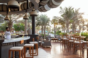 An outdoor bar area with wooden chairs and tables, surrounded by palm trees and a decorative ceiling with hanging lamps. - Jumeirah Al Naseem Dubai (Dubai)