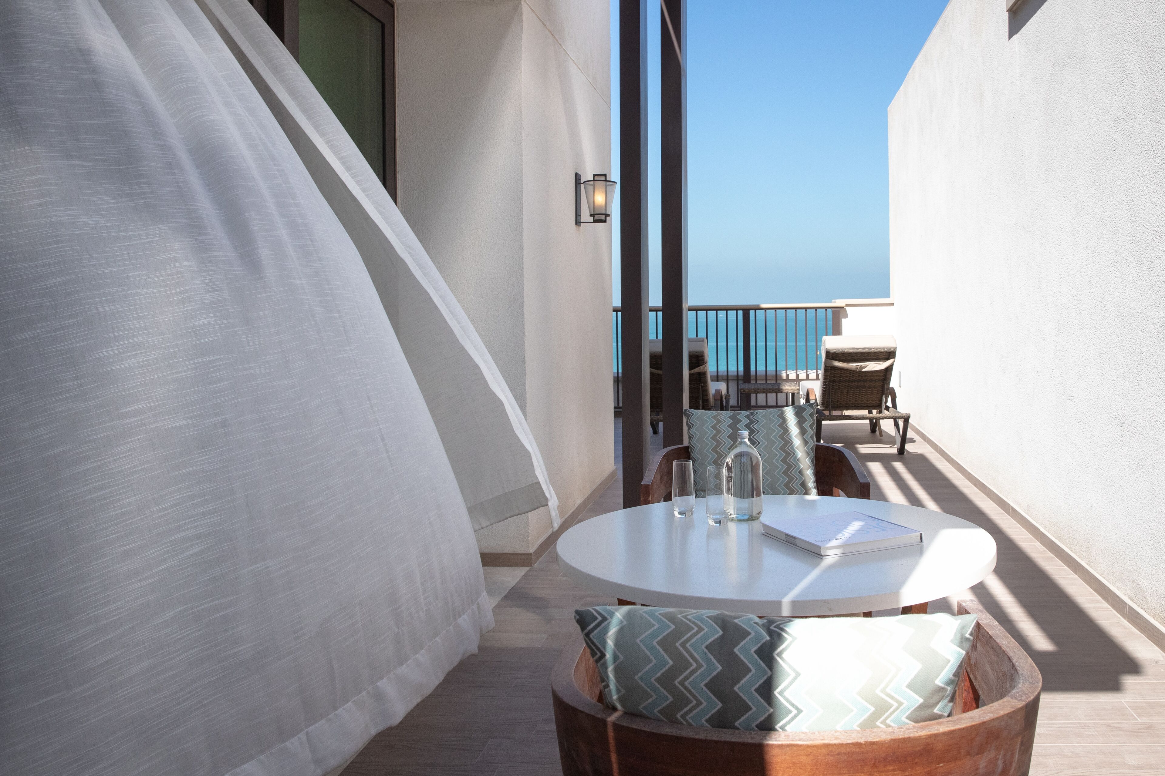 Un balcón con una mesa redonda, sillas y vista al mar.